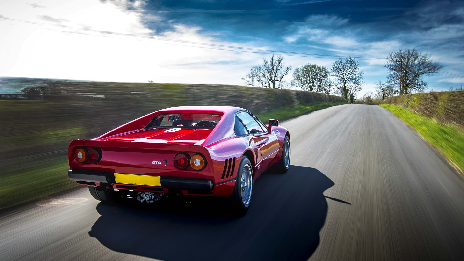 Classic red Ferrari 288 GTO speeding down a scenic country road. 