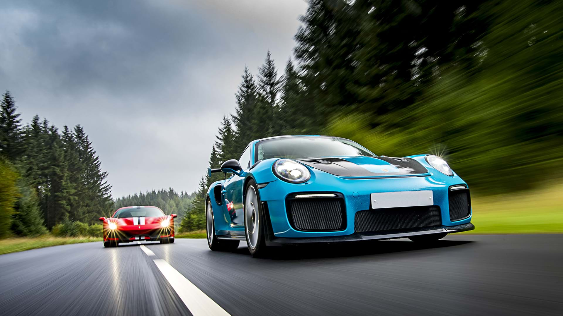 Blue Porsche 991 GT3 RS leading a red Ferrari 488 Pista on a scenic road. 